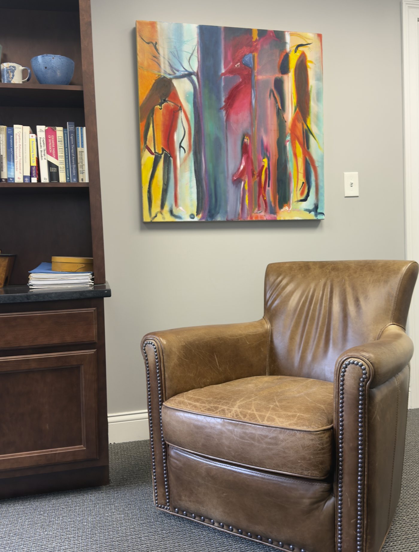 A consultation room at Integrative Psychiatry — leather chair beneath original artwork